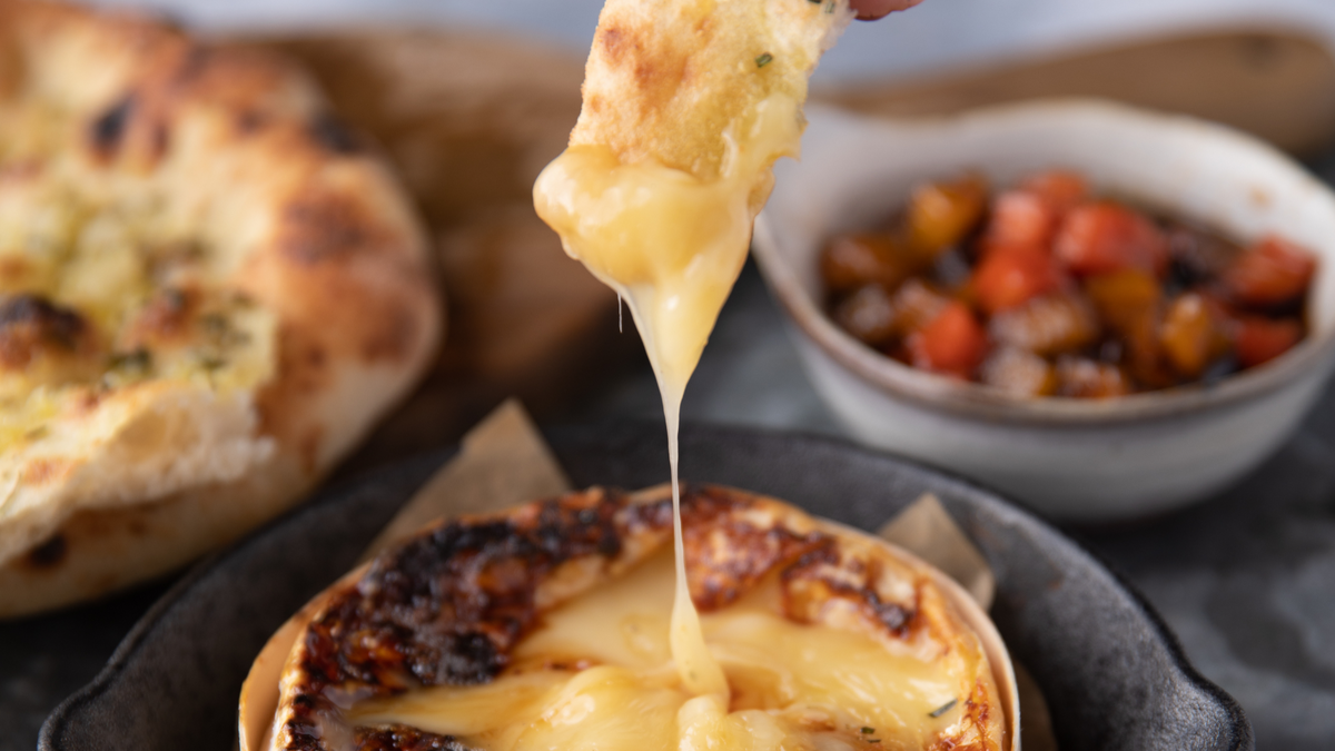 Baked Cheese being stretched out with jam and flatbreads in the background recipe poster image