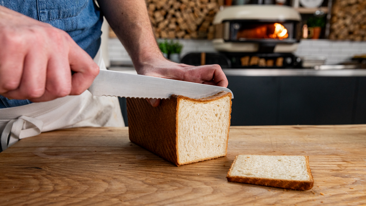 David Wright slicing a sandwich bread loaf in front of a Gozney Pizza Oven recipe poster image