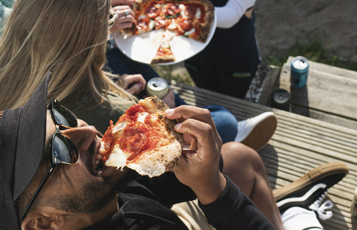 man taking a bite of pizza outside